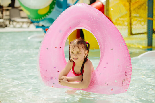 Girl relaxing on pink inflatable ring in water park pool
