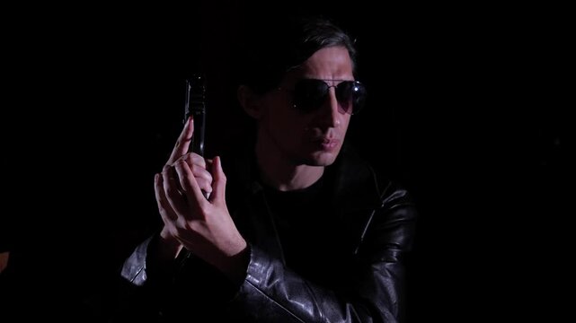 mid-shot captures a cool and mysterious mood as a man in a leather jacket and sunglasses holds a handgun, illuminated by a single light source against a dark background, suggesting a dramatic scenario