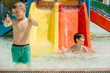 Children having fun on water slides at aqua park showing thumbs up sign