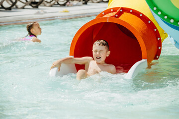 Child having fun sliding into waterpark pool on summer day