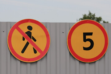 Two Round Yellow Road Signs On A Grey Corrugated Metal Wall: 