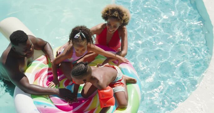 Diverse family balancing on donut float and arm floaties in pool after father's push