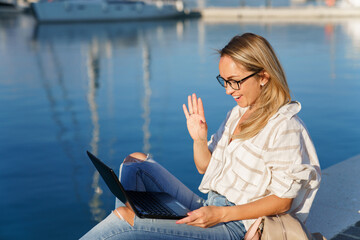 Woman working on vacation with laptop on sea beach. Online meeting call, video chat on travel,...