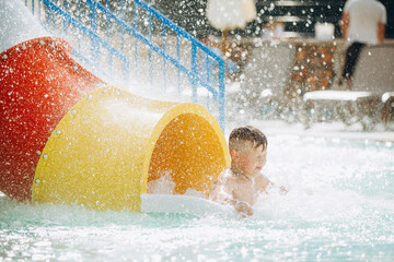 Child having fun exiting a colorful waterslide in a swimming pool
