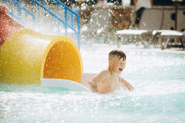 Happy child exiting water slide in aqua park pool