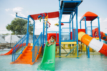 Girl sliding down water slide in colorful aqua park enjoying summer vacation