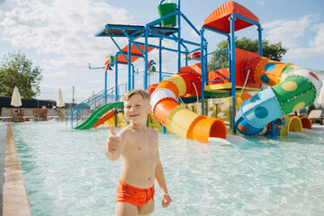 Child gesturing thumbs up in water park pool with slides