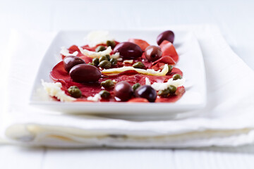 Slices of beef carpaccio with olives and capers. Close up.	