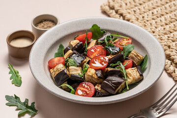 Eggplants tomatoes arugula salad in gray bowl on light beige background. Vegetarian summer Mediterranean salad