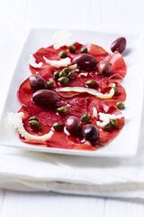 Slices of beef carpaccio with olives and capers. Close up.	