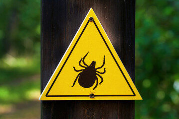 Yellow tick hazard signs on wood to protect outdoor visitors from health risks. Warning sign with black tick symbo, indicating potential risk of tick bites in forested outdoor settings, or city park © Tricky Shark