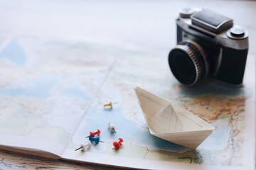 vintage camera, a handmade paper boat, and colorful push pins placed on a world map. This conceptual travel with copy space.