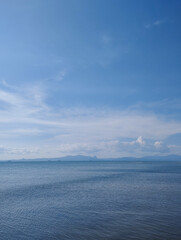 Daytime seascape with calm ocean water, clear blue sky, and scattered clouds. Peaceful and tranquil coastal scenery.