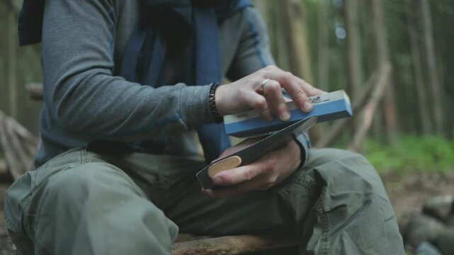 A man sharpens his axe deep in the forest. Sustainable survival concept focused on eco-friendly tools and living in harmony with nature.
