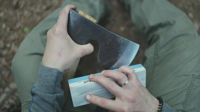 A man sharpens his axe deep in the forest. Sustainable survival concept focused on eco-friendly tools and living in harmony with nature.