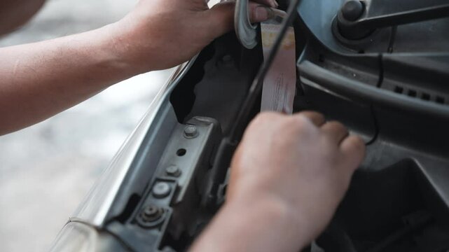 A man is rubbing the chassis number area under the hood of a car to make a chassis number impression for verification or registration purposes. Gesek no rangka