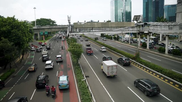 &lrm;Jakarta, Indonesia - &lrm;May 30, 2025: Heavy traffic fills a Jakarta street with cars and motorbikes under a pedestrian bridge connected to a TransJakarta bus stop.