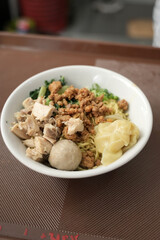 A bowl of Indonesian chicken noodles with chicken pieces, meatballs, dumplings and vegetables, served with separate broth.