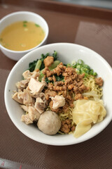 A bowl of Indonesian chicken noodles with chicken pieces, meatballs, dumplings and vegetables, served with separate broth.