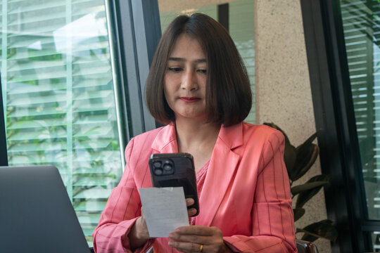 Woman sitting on chair and holding mobile phone document paper using scan barcode bill pay online internet banking,Technology of financial concepts