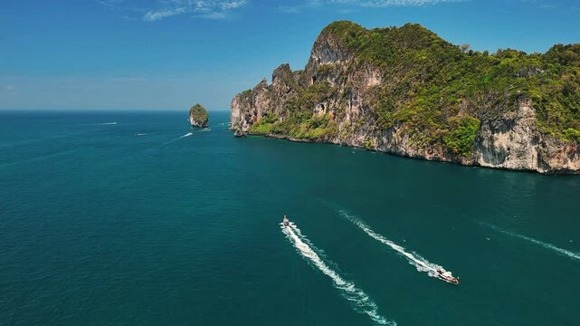 Aerial view of motorboats cruising through vibrant turquoise waters under a clear blue sky, Phi phi islands, Phuket, Thailand.