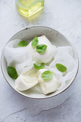 Bowl with freshly made buffalo mozzarella and green basil on a white stone background, elevated view, vertical shot