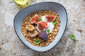 Granola bowl with fresh and dried figs and yogurt, horizontal shot on a light-brown granite surface, elevated view