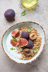 Bowl with granola, fresh and dried figs and greek yogurt, vertical shot on a beige granite background, elevated view