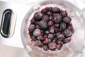 Frozen berries in blender. Icy wild blueberries and currants. Preparing smoothie at home. Healthy fruit for vegan breakfast. Top view composition in natural light. Cold detox ingredients ready.
