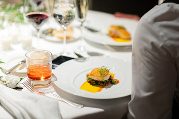plates of seared scallops with garnish on table with cocktails and wine at gourmet restaurant