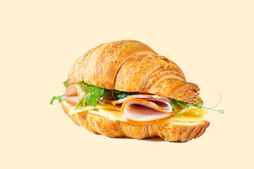 Croissant sandwich with cheese, ham and pea microgreens isolated on yellow.