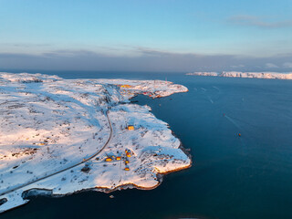 Panoramic aerial view of a snowy coastal village nestled among hills leading to the open sea in...