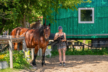Young woman leading beautiful brown horse on rural horse farm. Authentic moment of connection,...