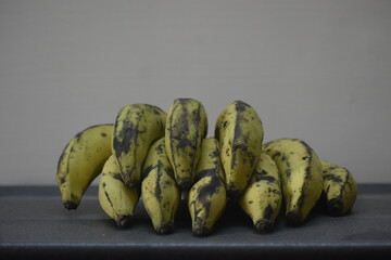 Naturally ripened, yellowish-green bananas with brown spots on a dark surface and plain background.