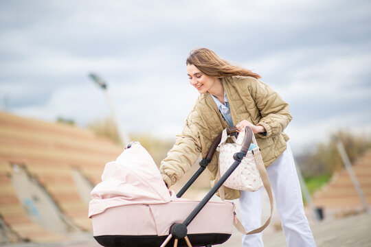 smiling young woman leans over a pink stroller to check on her baby during a walk