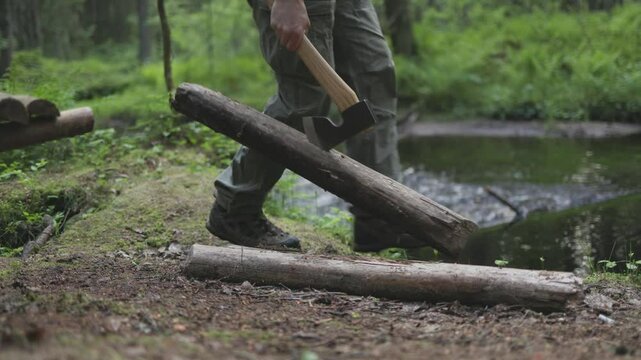 A man throws an axe into a log and grabs it, preparing firewood for survival. Eco-friendly wood gathering in the wilderness for forest survival.