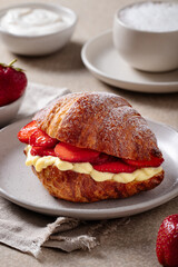 Croissant with strawberries and vanilla cream on plate with coffee and yogurt