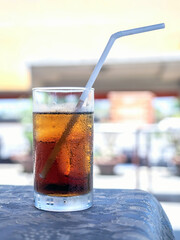Glass of refreshing cola with ice on table
