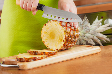 Woman chopping fresh pineapple on cutting board...