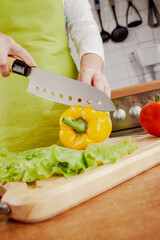 Woman chopping fresh yellow bell pepper on cutting board...