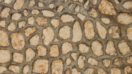 A rustic stone wall featuring irregularly shaped, light-colored rocks meticulously fitted together with dark mortar, forming a durable and textured surface.