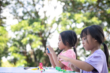 Obraz premium Two young girls are sitting at a table playing with clay