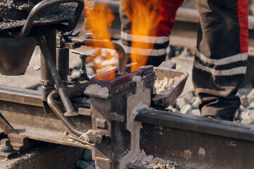 A worker in the process of a railroad track weld repair, reconstruction with a freight train passing