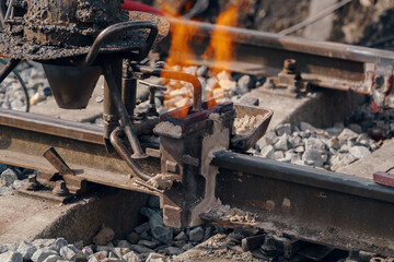 A worker in the process of a railroad track weld repair, reconstruction with a freight train passing