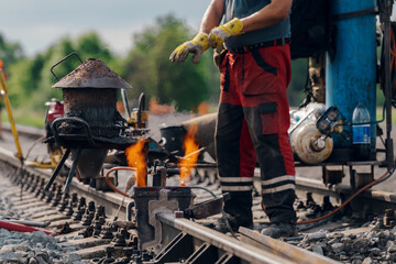 A worker in the process of a railroad track weld repair, reconstruction with a freight train passing