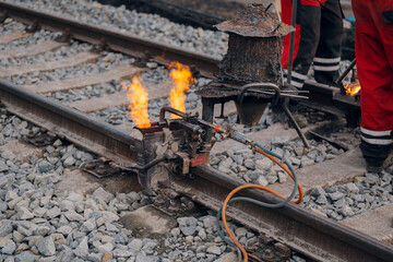 A worker in the process of a railroad track weld repair, reconstruction with a freight train passing