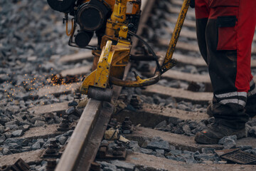 A worker in the process of a railroad track weld repair, reconstruction with a freight train passing