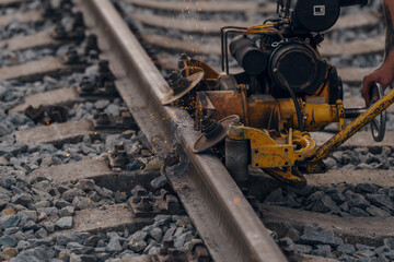 A worker in the process of a railroad track weld repair, reconstruction with a freight train passing
