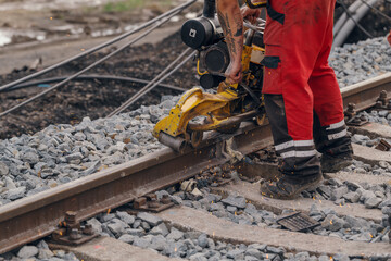 A worker in the process of a railroad track weld repair, reconstruction with a freight train passing