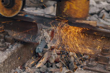 A worker in the process of a railroad track weld repair, reconstruction with a freight train passing